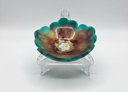 A small flower-shaped resin dish with a marbled pattern of green, brown, and gold, containing a small central gold inlay, photographed on a white sheet of paper.