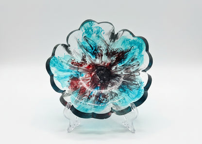 A flower-shaped translucent sun catcher with blue, black, and red patterns, placed on a white sheet of paper in direct sunlight.
