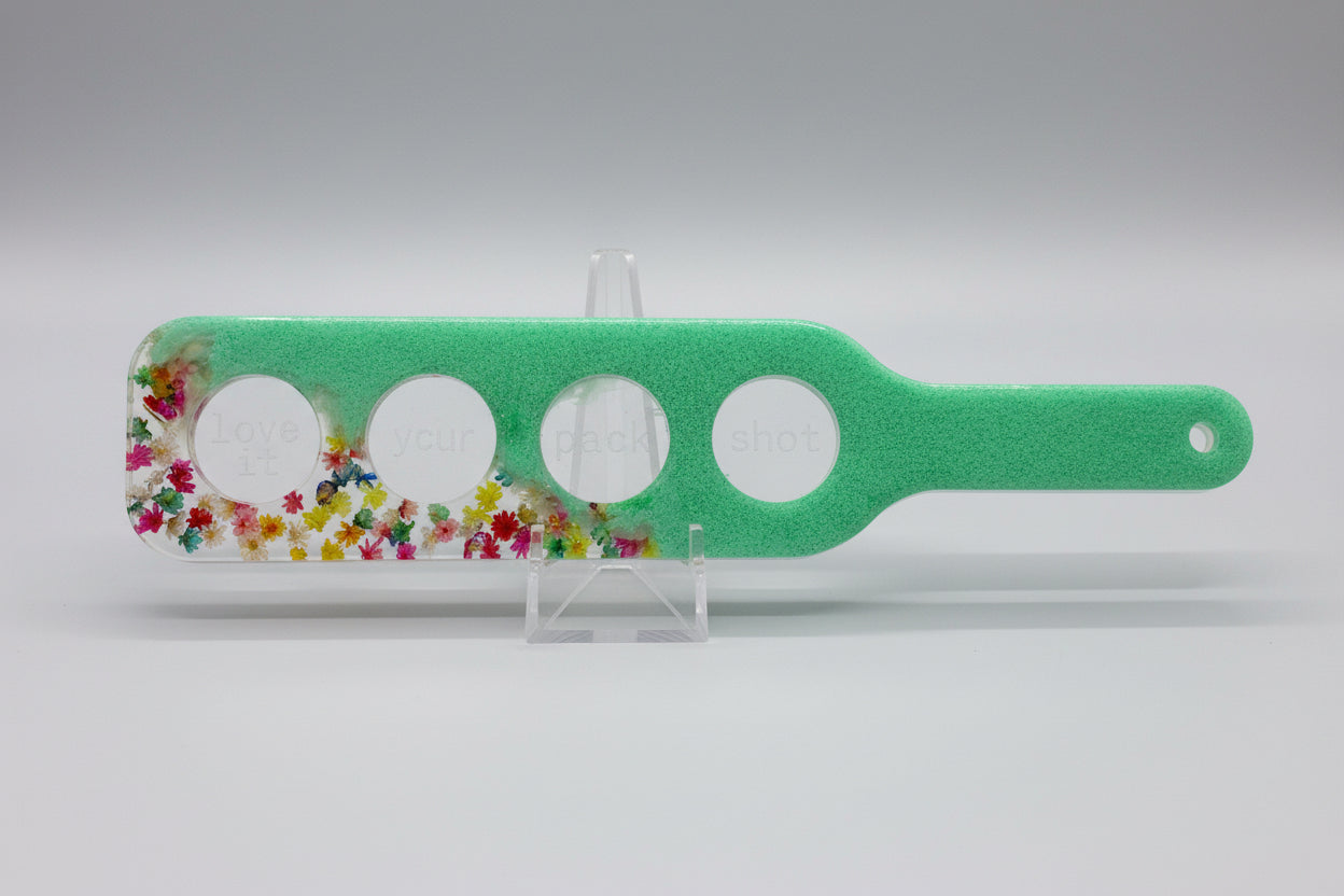A resin shot glass serving paddle with multi-color flowers and slots for four shot glasses.